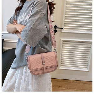 Detail of pink crossbody bag with woven texture flap and patterned wide shoulder strap