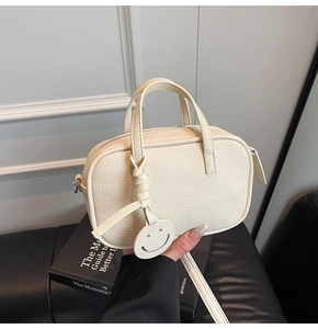 Detail of off-white lychee pattern pillow bag with cute smiley face charm and leather handles