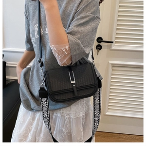 Close-up of black crossbody bag featuring woven texture flap and geometric pattern strap