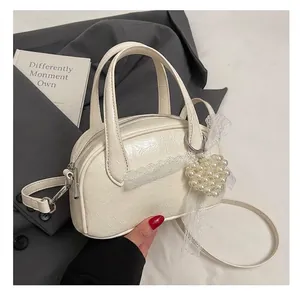 Détail du sac polochon en cuir crème avec pendentif décoratif en cœur de perle et dentelle
