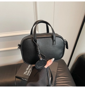 Detailed view of black lychee grain leather pillow bag with a round smiley face charm