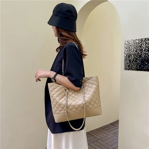 Beige quilted tote bag with chain strap and large capacity shown on a female model