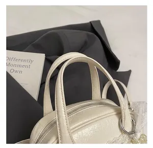 Gros plan d'un sac à main crème en cuir plissé avec poignées et breloque en perles