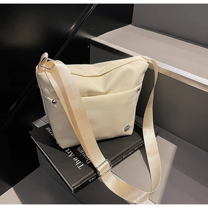 Détail du sac bandoulière en nylon crème avec logo métallique et sangle réglable
