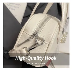 Détail du sac polochon crème avec texture craquelée, zip argenté et poignée de perles