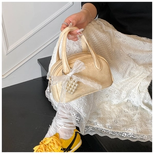 Détail d'un mini sac à main crème avec nœud en dentelle et breloques en perles