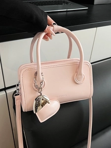 Chic pink leather crossbody handbag with round handles and a heart-shaped charm accessory