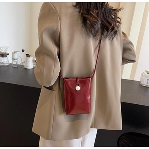 Detail view of burgundy leather small crossbody bag with pearl closure on khaki blazer