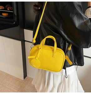 Close-up of a yellow pebbled leather phone bag with a smiley charm on a model