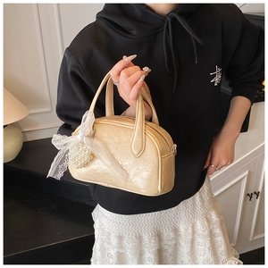 Détail du sac Boston crème avec un nœud en dentelle blanche et des breloques en perles