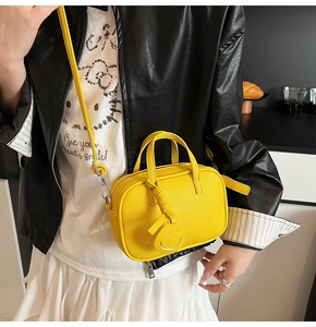 Detail of bright yellow leather mini crossbody bag with a round smiley face charm