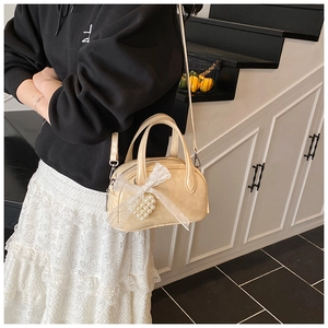 Détail du mini sac crème avec nœud en dentelle et breloque en perles en forme de cœur
