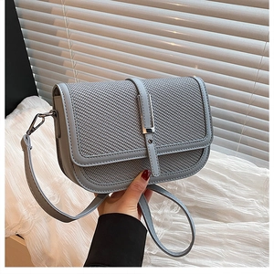 Close-up of light blue crossbody bag with woven texture flap and silver metal bar buckle
