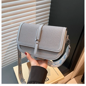 Detail of grey crossbody bag with woven texture flap and ethnic embroidery strap