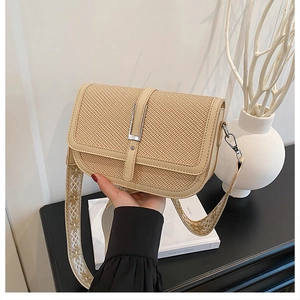 Detailed view of beige straw crossbody bag with wide embroidered strap on a desk