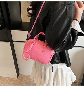 Detail of pink lychee leather handbag featuring a cute smiley face charm and shoulder strap