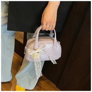 Détail du sac en cuir verni lavande avec un nœud en dentelle et un pendentif cœur