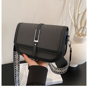 Close-up of black crossbody bag with woven texture lid and geometric strap detail