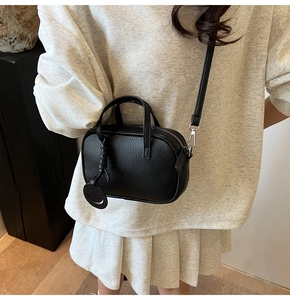 Detail of black litchi grain leather crossbody bag featuring a cute smiley face charm