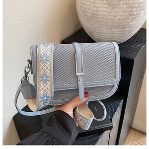 Detail of blue-grey crossbody bag with woven texture and jacquard floral strap