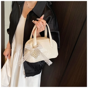 Détail du sac à main blanc cassé avec nœud en dentelle, pendentif perle et fermeture éclair