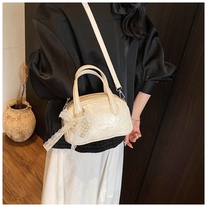 Détail d'un sac Boston beige à texture plissée brillante et breloque coeur en dentelle