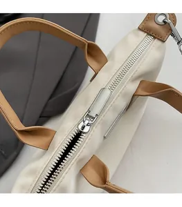 Detailed close-up of smooth silver metal zipper and brown leather handle on a beige tote bag