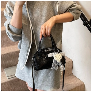 Détail d'un sac à main en cuir verni noir avec charm coeur en perles et dentelle