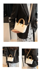 Detailed view of the beige bucket bag with brown leather handles and slim shoulder strap