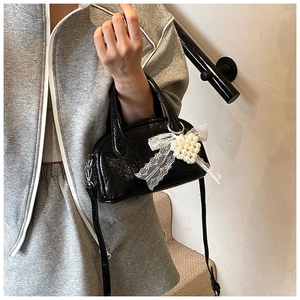Détail du sac à main noir brillant avec nœud en dentelle et cœur perlé sur mannequin