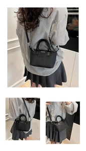 Detail view of the black nylon bucket bag featuring round handles and a metal logo plaque