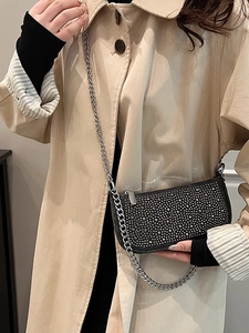 Chic black saddle bag with silver studs and chain strap worn over a beige coat