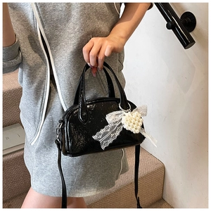 Détail du sac croissant noir verni avec nœud en dentelle et pendentif cœur perle