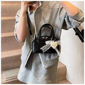 Détail du sac Boston en cuir verni noir avec nœud en dentelle et breloque en perle
