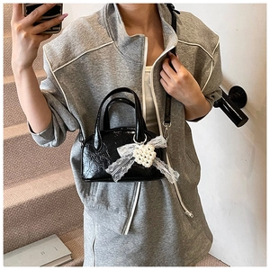 Détail du mini sac en cuir verni noir avec nœud en dentelle et pendentif perle