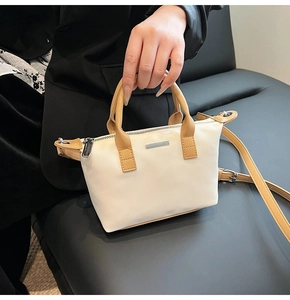 Detail of minimalist cream bucket bag showing brown leather handles and silver hardware