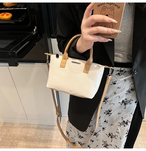 Detailed close-up of a minimalist cream bucket bag with metal bar trim and thin shoulder strap