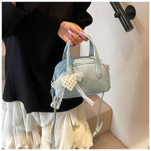 Détail du sac Boston bleu clair avec breloque cœur en dentelle et poignée texturée