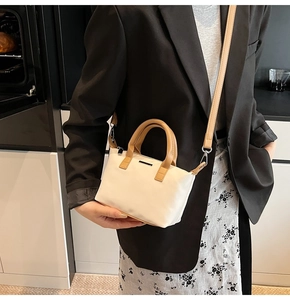 Detail of minimalist bucket bag showing cream leather, brown handles and metal logo plate