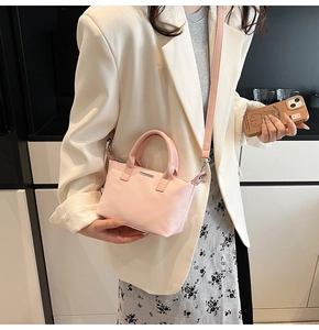Detail of light pink mini bucket bag with silver metal plate and top handle on model