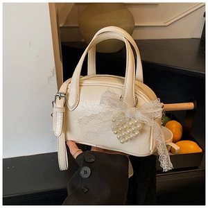 Détail du sac polochon blanc cassé en similicuir avec nœud en dentelle et cœur perlé