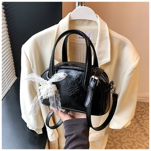 Détail du sac Boston noir en cuir verni plissé avec nœud en dentelle et perle