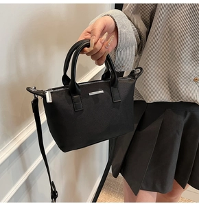 Detail of black nylon bucket bag with silver metal plaque and faux leather handles
