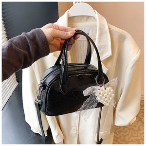 Détail du sac noir brillant avec breloque cœur en perle et nœud en dentelle