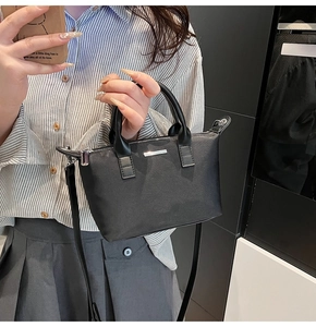 Detail of a black minimalist bucket bag featuring leather handles and silver metal logo plate