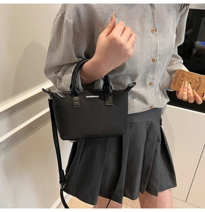 Close-up of black nylon bucket bag featuring leather handles and metal brand plate