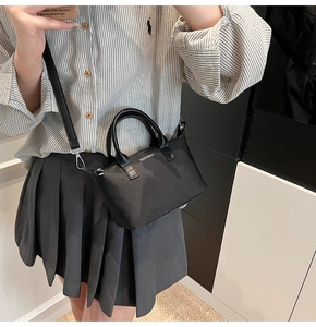Detail of a black nylon bucket bag featuring synthetic leather handles and a long strap