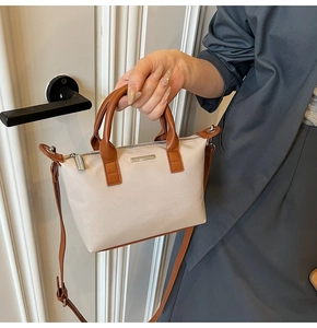Close-up of beige and brown bucket bag with metallic plate and adjustable shoulder strap