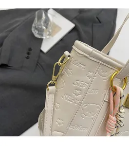 Detail of creamy white bucket bag featuring embossed bear patterns and gold hardware hook