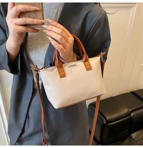 Detail of minimalist bucket bag with cream canvas, brown leather handles and metal logo